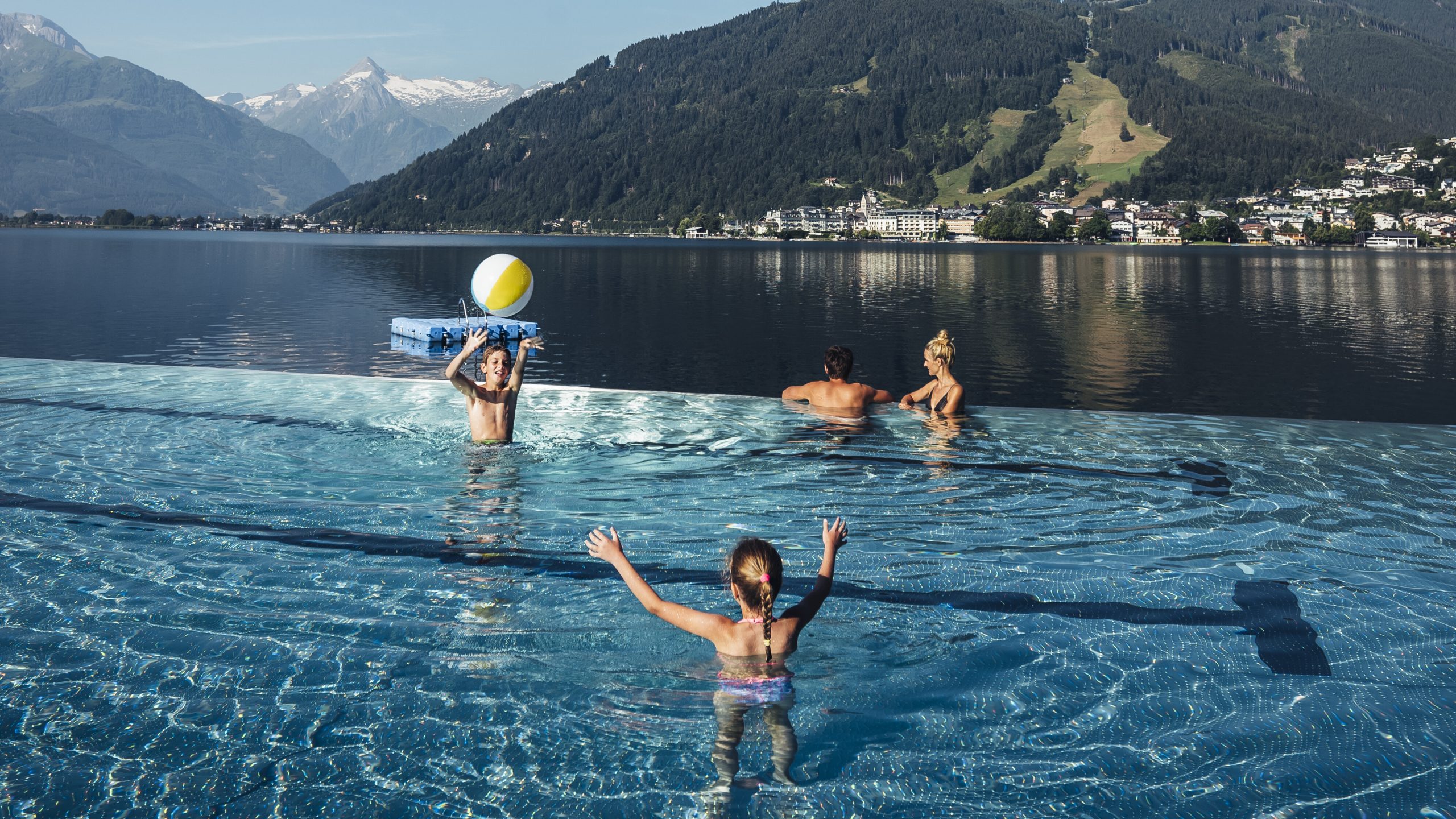 Familie im Sommerurlaub im Schwimmbecken im Thumersbacher Strandbad mit Blick auf den See und die Schmittenhöhe