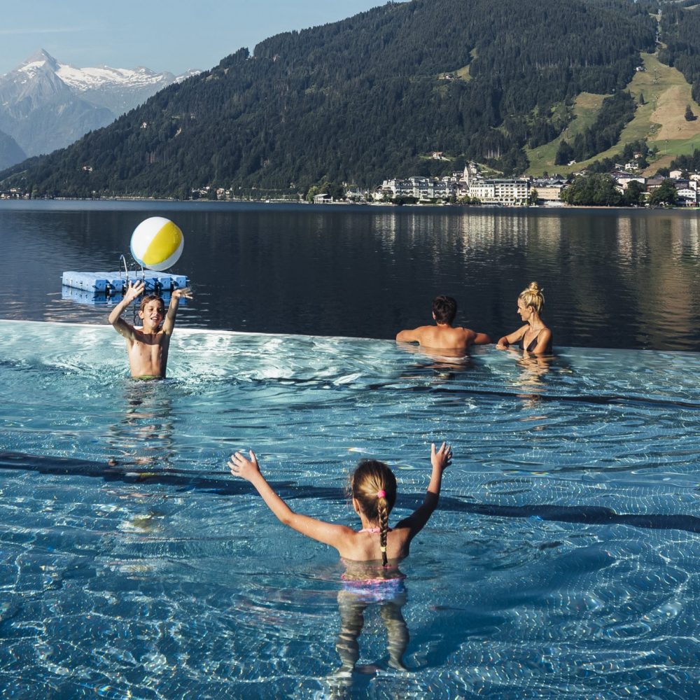 Familie im Sommerurlaub im Schwimmbecken im Thumersbacher Strandbad mit Blick auf den See und die Schmittenhöhe